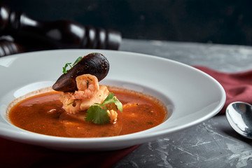 Fresh seafood soup in a white plate on dark background, side view