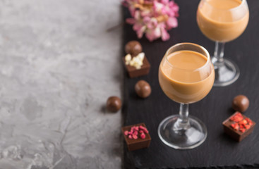 Sweet chocolate liqueur in glass on a gray concrete background and black stone slate board. Side view, copy space.