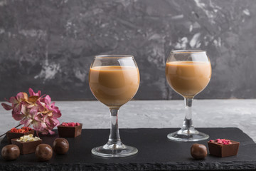 Sweet chocolate liqueur in glass on a gray concrete background and black stone slate board. Side view.