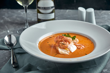 Fresh seafood soup in a white plate on dark background, side view