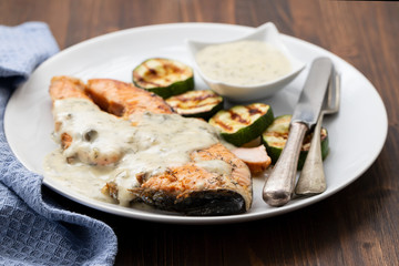 fried salmon with sauce and vegetables on white dish on brown wooden background. top view.