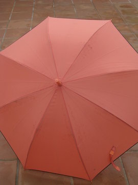 paraguas abierto,femenino grande tono rosa anaranjado (color salm&oacute;n) brillante para alegrar el d&iacute;a gris,  mojado en terraza de baldosas en d&iacute;a de lluvia y fr&iacute;o