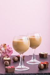 Sweet chocolate liqueur in glass with chocolate candies on a pink background and black stone slate board. Side view, copy space.