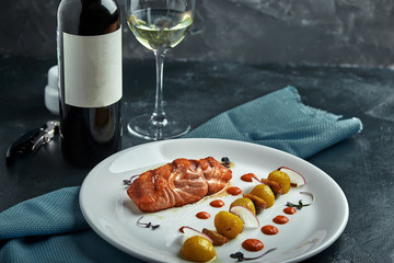 A large roasted piece of red fish lies on a white plate with vegetables, a beautiful serve in a restaurant