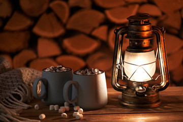The antique oil lamp and mugs with hot cocoa on the firewood background.