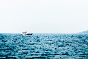 A fisherman boat floating in the sea. With the blue sea in contrast to the white sky.