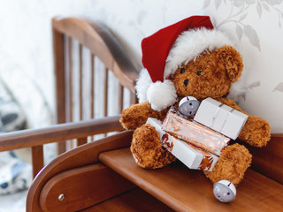 Teddy bear in Santa Claus hat. Plush toy with Christmas presents wrapped in white and golden paper. Kids room before New Year.