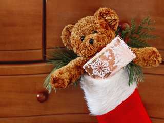 Brown teddy bear in red Santa Claus sock. Plush toy with Christmas present.  New Year gift in bright golden paper.