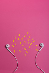 white earphones and yellow paper notes on pink background. view from above.