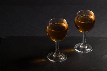 Glass of whiskey on a black stone slate board on black background. Side view, low key, copy space.