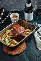 Roasted pork neck with baked potatoes and herbs on a tray on the black background