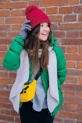 Woman hipster in bright clothes laughing and smiling. Young happy girl in a red knit hat, green jacket, grey scarf, yellow small bag. Women's fashion.