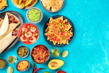 Mexican food, a flat lay top shot on a blue background with a place for text. Nachos, quesadillas, guacamole, chili con carne, burritos, and a shrimp cocktail, tequila and lime, with copyspace