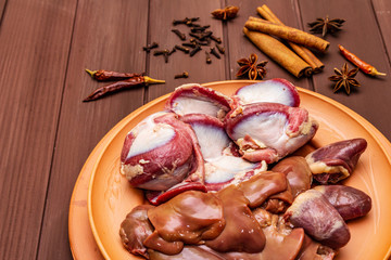 Fresh raw duck offal: heart, liver, stomach. Dry spices: cinnamon, star anise, clove, chili pepper. Wooden boards background