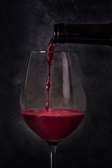 Pouring wine into a glass from a bottle, a close-up on a dark background
