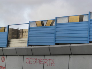 vallas azules de puente con una pared eliminada que deja ver casas de la ciudad y dos vallas con parte de grafitis , mensaje "despierta" en la ciudad. Grafiteros urbanos. fondo de cielo nublado gris