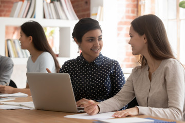 Smiling young indian student considering college assignment with groupmate.