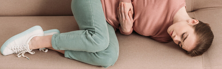 panoramic shot of unhappy woman lying on sofa while suffering from stomach pain