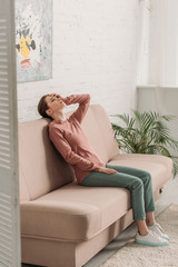 young woman sitting on sofa and looking up while suffering from headache