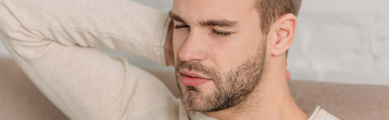 Fototapeta premium panoramic shot of man with closed eyes sitting on sofa and suffering from neck pain