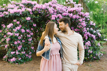 A beautiful couple in love on the background of bright flowering rhododendrons look at each other. Valentine's day