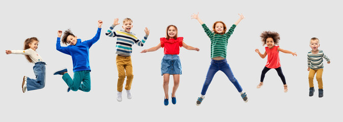 childhood, motion and happiness concept - happy little children jumping in air over grey background