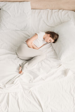 top view of girl lying in bed with closed eyes and suffering from abdominal pain