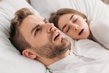 Fototapeta na wymiar awakened man looking up while lying in bed near snoring wife