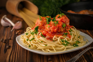 Close-up a plate of spaghetti with meatballs in tomato sauce and raw spaghetti with a frying pan in the background