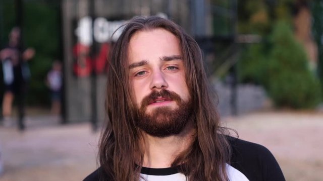 Close up, Portrait of a handsome Caucasian bearded young man with long looking artistic at camera in the sunset forest. Side view