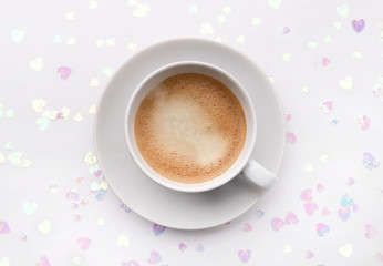 Holographic glitter confetti in heart shape and cup of coffee on white background