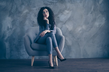 Portrait of her she nice-looking attractive charming classy minded wavy-haired girl psychologist sitting in chair crossed legs thinking about finance invest gray concrete wall background