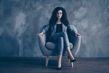 Fototapeta na wymiar Portrait of her she nice-looking attractive pretty classy chic content serious authoritative wavy-haired girl sitting in chair crossed legs gray concrete wall background