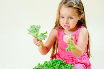 Cute little girl in a pink dress holding fresh lettuce on a light background. The concept of proper nutrition, vegetarianism. Copy space
