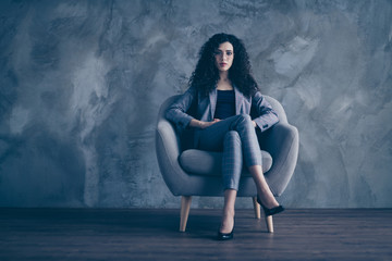 Portrait of her she nice-looking attractive classy chic content serious wavy-haired girl hr director finance sitting in chair waiting meeting appointment gray concrete wall background