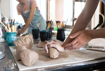A Potter girl kneads a piece of clay with her hands in her Studio workshop. - obrazy, fototapety, plakaty