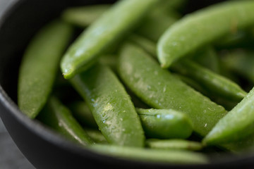vegetable, food and culinary concept - close up of peas in bowl on wet slate stone background