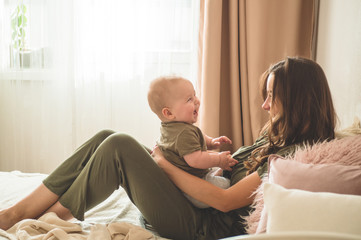 Home portrait of a baby boy with mother on the bed. Mom holding and kissing her child. 