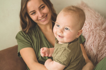 Home portrait of a baby boy with mother on the bed. Mom holding and kissing her child. 