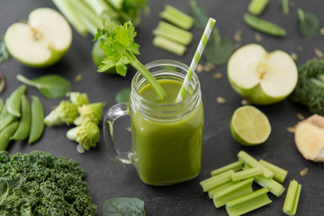 healthy eating, food and vegetarian diet concept - close up of glass mug of fresh green juice or smoothie with paper straw, fruits and vegetables on slate stone background