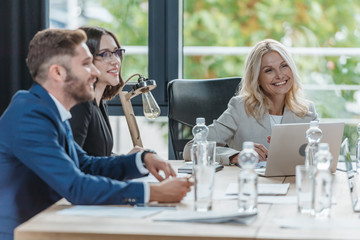 cheerful businesspeople sitting in meeting room near desk with documents and bottles of water