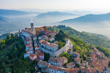 Ancient city Motovun on top of the mountain.The city is surrounded by a fortress wall.The background image are mountains and fog at the foot of the mountains. Istria, Croatia.The view from the drone.  - obrazy, fototapety, plakaty