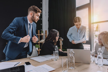 young businesspeople talking during business meeting near desk with digital devices and documents