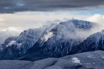 Fototapeta premium Beautiful mountain panorama in winter with fog and clouds. Bucegi mountains seen from Postavaru, Romania.
