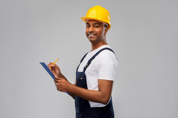 profession, construction and building - happy smiling indian worker or builder in helmet with clipboard and pencil over grey background