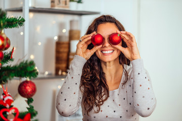 Close-up portrait of a goofy woman holding red ball ornaments as eyes during Christmas time.