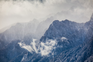 Beautiful mountain panorama in winter with fog and clouds. Bucegi mountains seen from Postavaru, Romania.