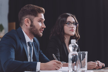 young businessman writing in notebook near attractive colleague