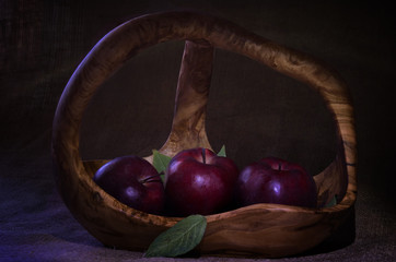 Red apples with few green leaves in wooden basket