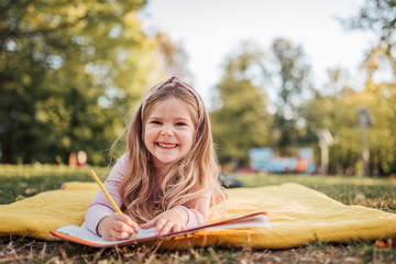 Outdoor portrait of a cute blonde child lying on the ground, smiling at camera.